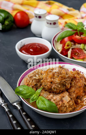 Fleischbällchen in saurer Sahne Sauce und frisches Gemüse Salat in Schalen gegen einen dunklen Hintergrund, vertikale Ausrichtung Stockfoto