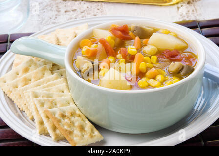 Warme Hausgemachte Gemüsesuppe und serviert mit knusprigen saltine Cracker in einem hellen Blau Schüssel auf eine weiße Platte. Stockfoto