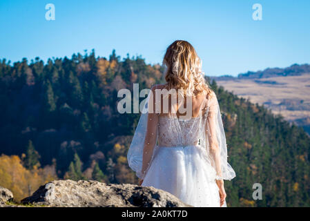 Rückseite der Braut im weißen Kleid auf die Berge bei Sonnenuntergang. Stockfoto