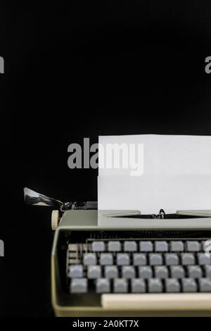 Schreibmaschine Auf dem Tisch auf einem schwarzen Hintergrund mit weißen Papier mit leeren Raum. Arbeitsplatz der Autorin oder Autor. Idee, Konzept. Stockfoto