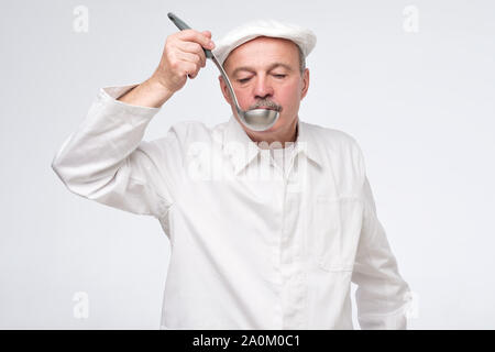 Kochen, Beruf und Menschen anhand von quantitativen Simulatio. Männliche Koch Küchenchef in weiße Uniform Geschmack von Kelle. Studio shot Stockfoto