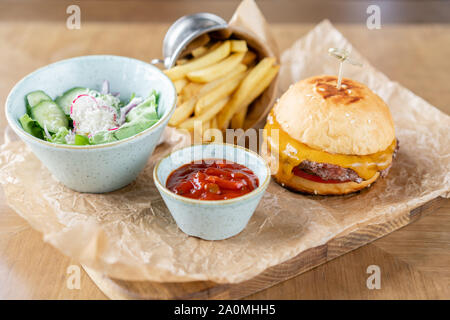 Ungesunde Lebensmittel. Cheeseburger mit Salat, Tomaten, Pommes frites und geschmolzenem Käse. Der Tisch im Restaurant. Stockfoto