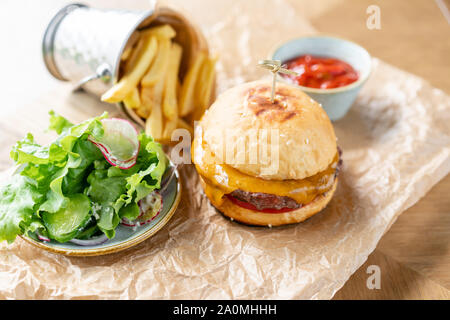 Ungesunde Lebensmittel. Cheeseburger mit Salat, Tomaten, Pommes frites und geschmolzenem Käse. Der Tisch im Restaurant. Stockfoto