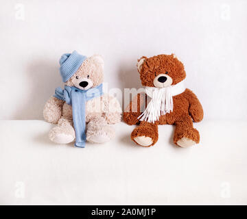 Kinder Spielzeug Teddybären sitzen auf einem weißen Sofa in einem gestrickt, weißen und blauen Schal und Hut. Selektive konzentrieren. Stockfoto