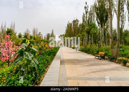 Hotan malerischen Kunlun Lake Park Blick auf Blume Garten Gasse mit Bänken sitzen und nur wenige Menschen an einem bewölkten Himmel Tag Stockfoto