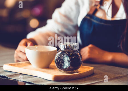 Nahaufnahme des Professional Female barista Hand und halten weiße Tasse Kaffee. Glückliche junge Frau an der Bar im Restaurant Hintergrund. Menschen Stockfoto