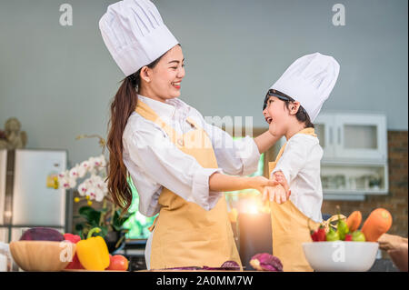 Gerne schöne asiatische Frau dress up niedlichen kleinen Jungen Küchenchef Outfit für zum Kochen in der Küche zu Hause vorbereiten. Menschen Lebensstile und Familie. Hausgemachte Speisen ein Stockfoto