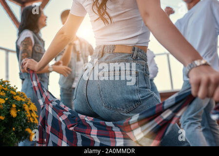 Nahaufnahme Foto einer Frau in Freizeitkleidung Holding kariertem Hemd hinter zurück beim Stehen auf Dachterrasse mit ihren Freunden. Party Konzept. Freundschaft Stockfoto