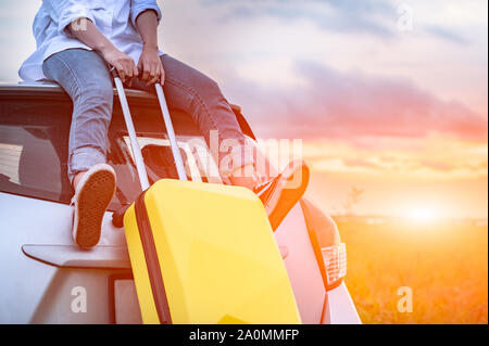Nahaufnahme der glücklichen asiatischen Frau an der Spitze der auto mit Gepäck Tasche. Mädchen sitzt auf dem Dach und suchen Sonnenuntergang vor Abend. Menschen Lebensstil in Langen Urlaub Stockfoto