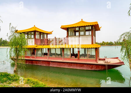 Hotan malerischen Kunlun Lake Park Blick auf einen Verankerten chinesisches Schiff am Ufer an einem bewölkten Himmel Tag Stockfoto