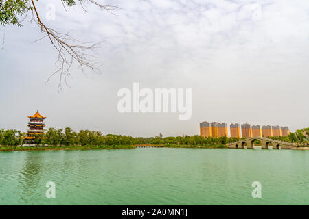 Hotan malerischen Kunlun Lake Park Blick auf Pagode auf der Insel und Verbeugte sich Stone Bridge an einem bewölkten Himmel Tag Stockfoto
