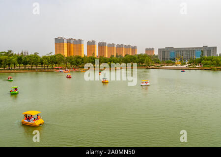 Hotan malerischen Kunlun Lake Park Blick auf Segelboote mit Menschen- und Wohngebäude im Hintergrund an einem bewölkten Himmel Tag Stockfoto