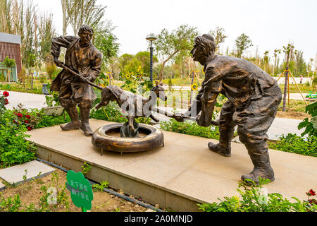 Hotan malerischen Kunlun Lake Park Blick auf eine Statue von zwei uigurische Männer Grillen ein Lamm über im Tandoori Ofen an einem bewölkten Himmel Tag Stockfoto