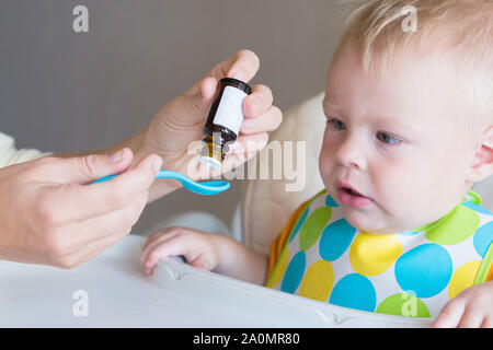 Vitamine für junge Kinder. Mom tropfen Vitamine in einem Löffel, während ihr kleiner Sohn einziehen. Gesunde Kindheit. Stärkung und Schutz gegen Dis Stockfoto