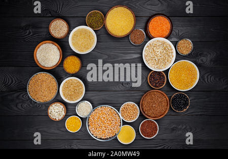 Runden Rahmen von Getreide, Körner, Samen, Grütze, Hülsenfrüchte und Bohnen in Schalen, ballaststoffreiche Ernährung Konzept, Ansicht von oben porridge Sammlung auf schwarzem Holz- ba Stockfoto