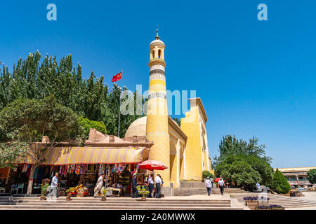 Kashgar Id kah-Moschee mit einem Winkenden China Flagge auf dem Dach und uigurische Männer mit Doppa Hut auf ihren Kopf auf einem sonnigen blauen Himmel Tag Stockfoto