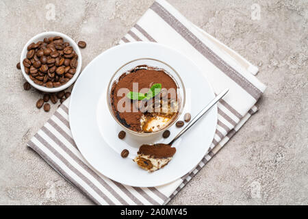 Teil der klassischen Tiramisu Dessert im Glas Schale auf konkreten Hintergrund Stockfoto