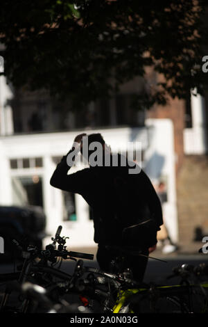 Ein junger Mann alter Anfang 30 geht weg vom Bike Rack, wo er sein Fahrrad verlassen hat. Silhouette. Aus Fokus Mann. Bike Rack ausgerichtet. Schatten Stockfoto