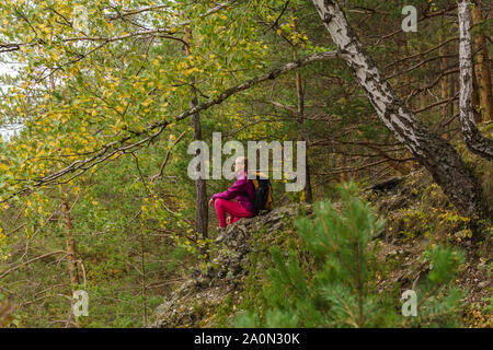 Junge Frau Wanderer sitzt auf einer Klippe unter den Herbst Bergwald Stockfoto