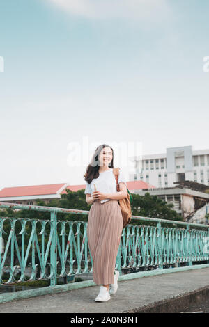 Schöne Asiatische weibliche Studenten ihre Bücher steht und Kleider bis Holding in Street fashion Tuch im Freien öffentlichen Raum mit modernen Gebäude ba Stockfoto