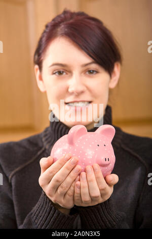 Junge Frau mit ihrem Einsparungen in einem rosa Sparschwein Stockfoto