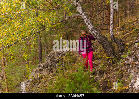 Weibliche Wanderer mit Rucksack vorsichtig macht sich auf den Weg entlang einer Mountain Trail unter den Herbst Wald Stockfoto