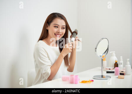 Das Loswerden von Kabelsalat. Schöne junge Frau an ihr Spiegelbild in mirrorand ihr langes Haar bürsten Während am Tisch sitzen Stockfoto