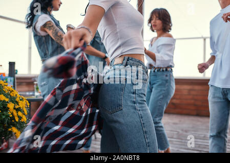 Nahaufnahme Foto einer Frau in Freizeitkleidung Holding kariertem Hemd hinter zurück beim Stehen auf Dachterrasse mit ihren Freunden. Party Konzept. Freundschaft Stockfoto