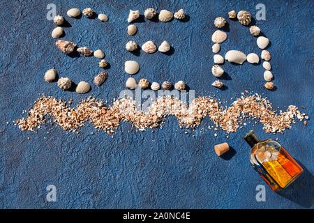 Wort Meer aus Muschelschalen, dekorative sea wave, goldener Sand, farbigem Glas Flasche mit Korken auf blauem Hintergrund der Ansicht von oben, Sommerferien Stockfoto