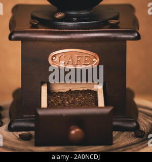 Nahaufnahme einer traditionellen Kaffeemühle mit Schublade voller gemahlenen Kaffee auf einer Holzoberfläche Stockfoto
