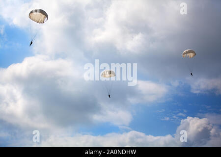 Drei Fallschirmjäger springen mit Fallschirmen auf dem blauen Himmel mit weißen Wolken Hintergrund Stockfoto