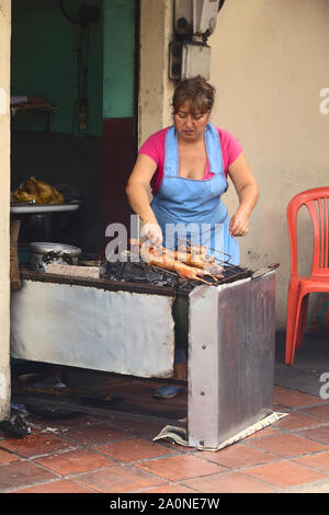 BANOS, Ecuador - 28. FEBRUAR 2014: Nicht identifizierte Frau rösten Meerschweinchen zum Verkauf an die Halle auf Ambato Straße in Baños, Ecuador Stockfoto