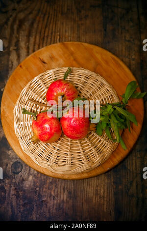 Rote reife Granatäpfel an wicker runde Platte. Studio gedreht. Stock Bild. Stockfoto