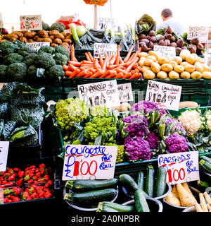 Markt Verkäufer der Verkauf von frischem Gemüse, einschließlich Romanisco, Lila Blumenkohl, Zucchini, Karotten, Kartoffeln, Kohl, Pastinaken und Rote Beete Stockfoto