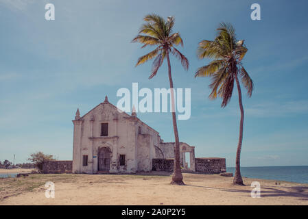 Eine alte verwitterte weiß getünchten Kirche am Strand der Insel von Mosambik (Ilha de Mocambique), mit zwei Palmen im Vordergrund. Nampula Pro Stockfoto