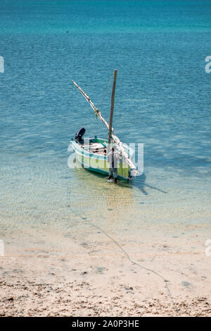 Insel Mosambik / Mosambik - 8. Juli 2019: ein Fischer in einem kleinen Fischerboot im seichten Wasser am Strand vertäut. Provinz Nampula, Afr Stockfoto