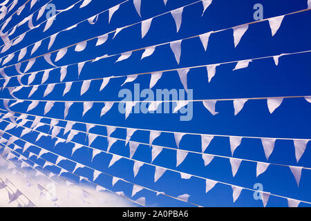 Weiße, dreieckige Fahnen schwenkten in Wind und blauer Himmel close up, Banner Klappe auf Brise, dekorative Kränze in der Luft, schöne Flaggen Linien Stockfoto