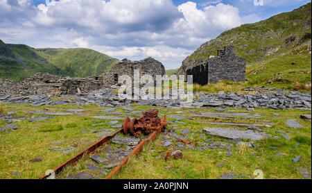 Verlassene und verfallene Schieferabbau Gebäude stehen inmitten von Geröll Tipps und die moelwyn Berge im Tal über Cwmorthin Blaenau Ffestiniog in Sn Stockfoto