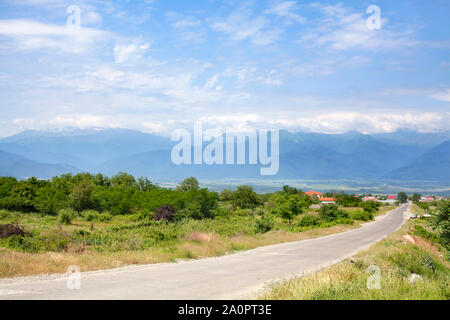 Leere Straße in die Landschaft, die Berge am Horizont und ein blauer Himmel mit Wolken Hintergrund Stockfoto