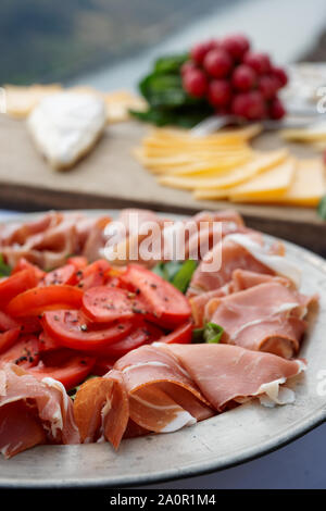 Platte mit Schinken auf Tisch, Rettich und Käse im Hintergrund Stockfoto