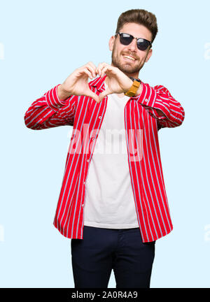 Junger stattlicher Mann mit Sonnenbrille in der Liebe mit Herz und mit Hand lächelnd. Romantische Konzept. Stockfoto