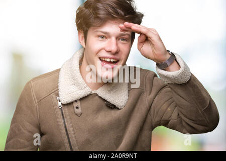 Jungen gutaussehenden Mann tragen Winter Mantel über isolierte Hintergrund sehr glücklich und lächelnd weit entfernt, mit der Hand über den Kopf. Suche Konzept. Stockfoto