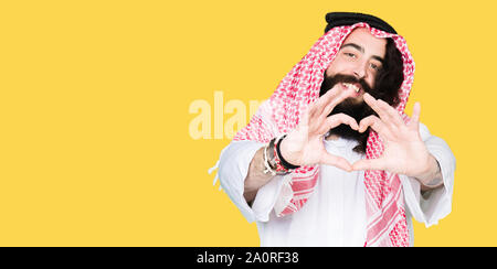 Arabian Business Mann mit langem Haar zu tragen traditionelle Kufiya Schal in der Liebe mit Herz und mit Hand lächelnd. Romantische Konzept. Stockfoto