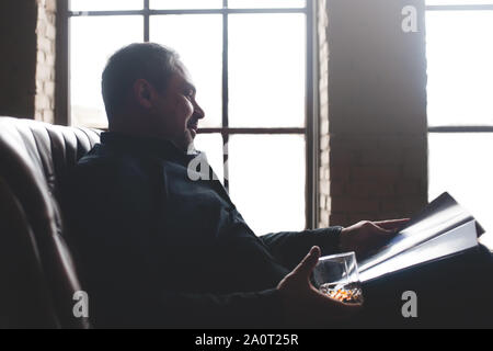 Eine entspannte Geschäftsmann ist ein teures trinken Trinken und Lesen einer Zeitschrift. Stockfoto