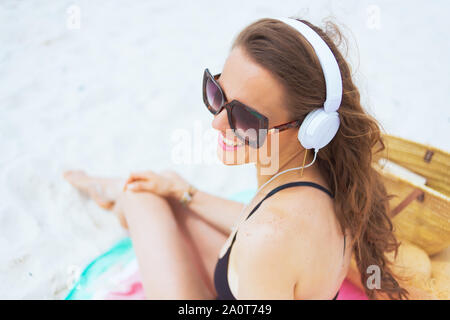 Obere Ansicht von Happy elegante 40-jährige Frau bei Sonnenbrillen die Musik mit Kopfhörern auf einem weißen Strand. Stockfoto