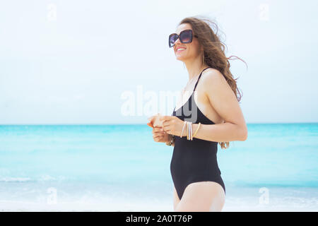 Gerne elegante 40-jährige Frau in Sonnenbrille mit Smartphone mit Anwendungen auf einem weißen Strand. Stockfoto