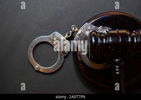 Handschellen und schwarzen Hammer auf schwarzem Hintergrund isoliert. Recht und Gesetz Konzept Stockfoto