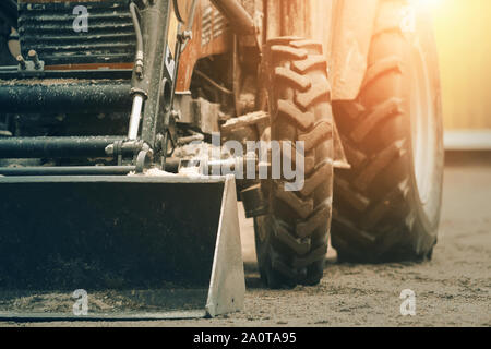 Eine riesige Schaufel und große Räder mit neuen Reifen auf der Bulldozer, stehend auf einem sandigen Oberfläche und durch Licht beleuchtet. Stockfoto