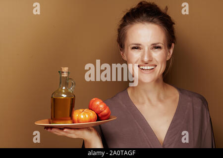Hallo Herbst. Portrait von Happy Elegant 40 Jahre alte Frau in einem Bademantel mit Kürbiskernöl gegen bronze Hintergrund. Stockfoto