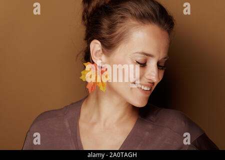 Hallo Herbst. lächelnd elegante 40-jährige Frau in einen Bademantel mit Herbst Blatt Ohrring auf braunem Hintergrund. Stockfoto